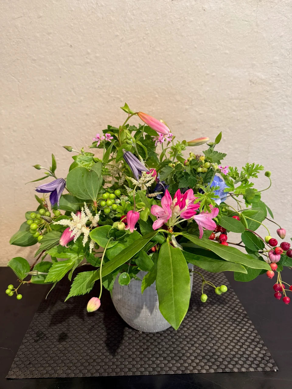 灰色の器にピンクや紫の季節の花と枝葉を合わせたアレンジメント